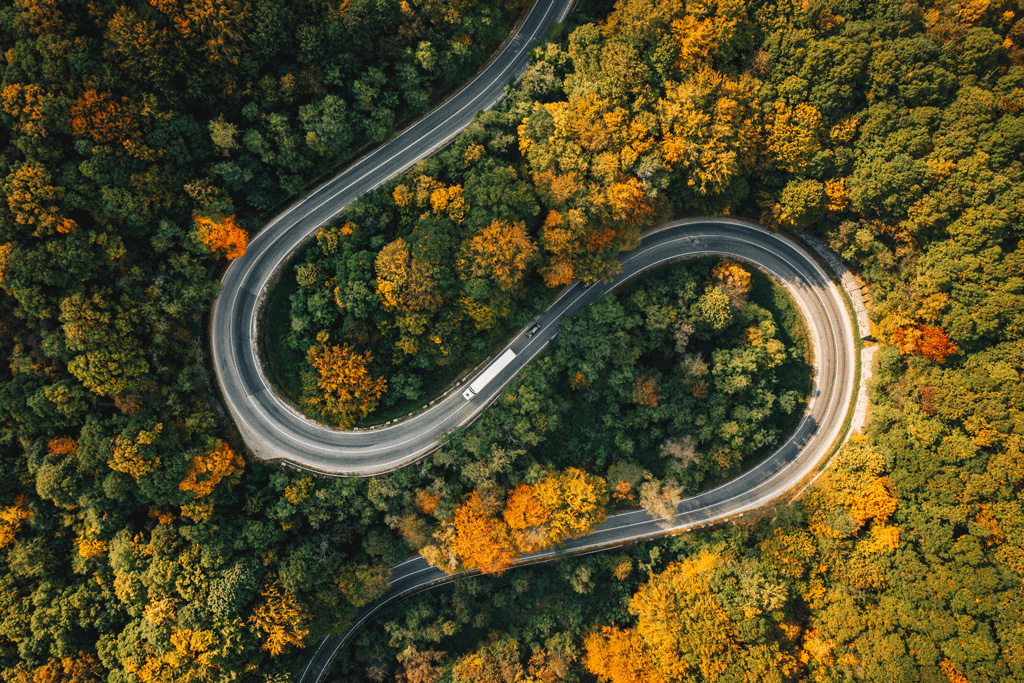 Een elektrische vrachtwagen rijdt op een kronkelige weg langs bomen in de herfst